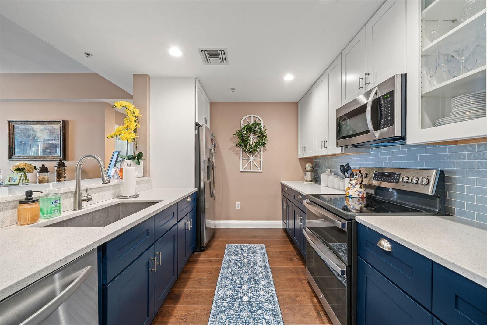 A kitchen features blue lower cabinets, white upper cabinets, stainless steel appliances, and a tile backsplash — 1203 Town Center Drive # 313, Jupiter FL 33458, JUPITER, FL