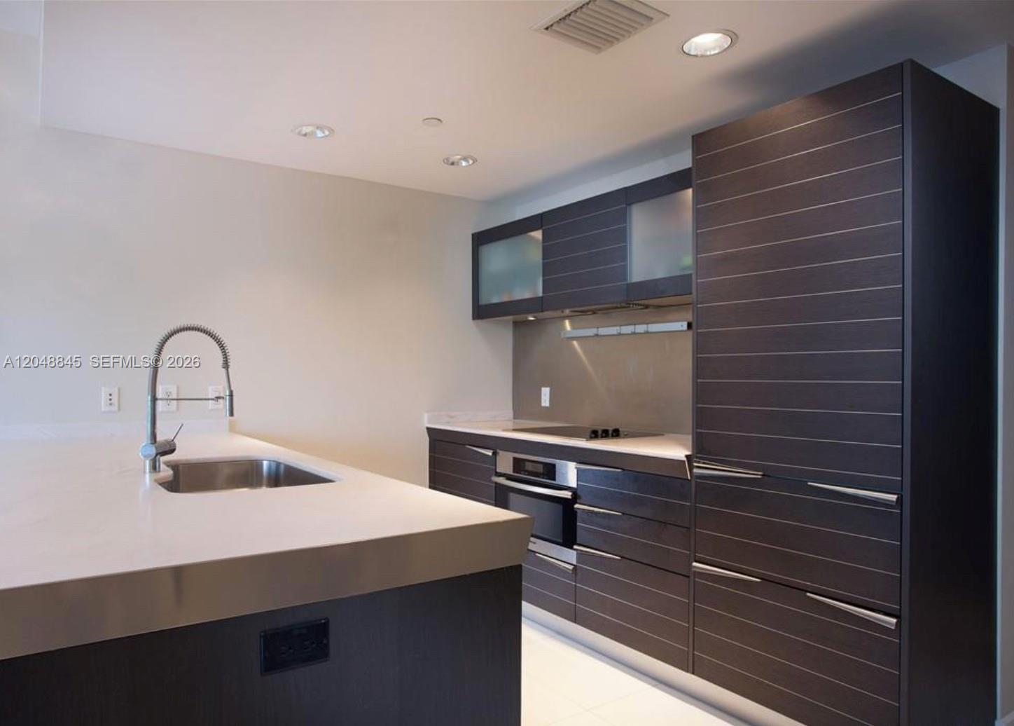 A modern kitchen features dark horizontal-paneled cabinetry, white countertops, and a stainless steel sink — 200 Biscayne Boulevard Way # 3209, Miami FL 33131, MIAMI, FL