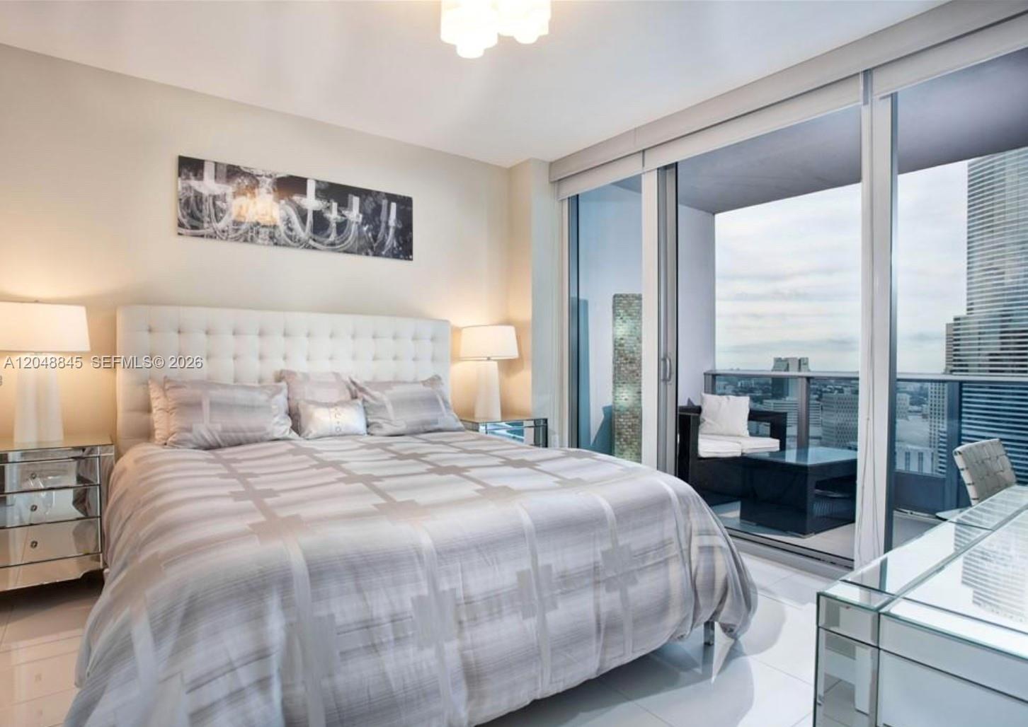 A modern bedroom features a tufted headboard, mirrored nightstands, and a balcony with city views — 200 Biscayne Boulevard Way # 3209, Miami FL 33131, MIAMI, FL