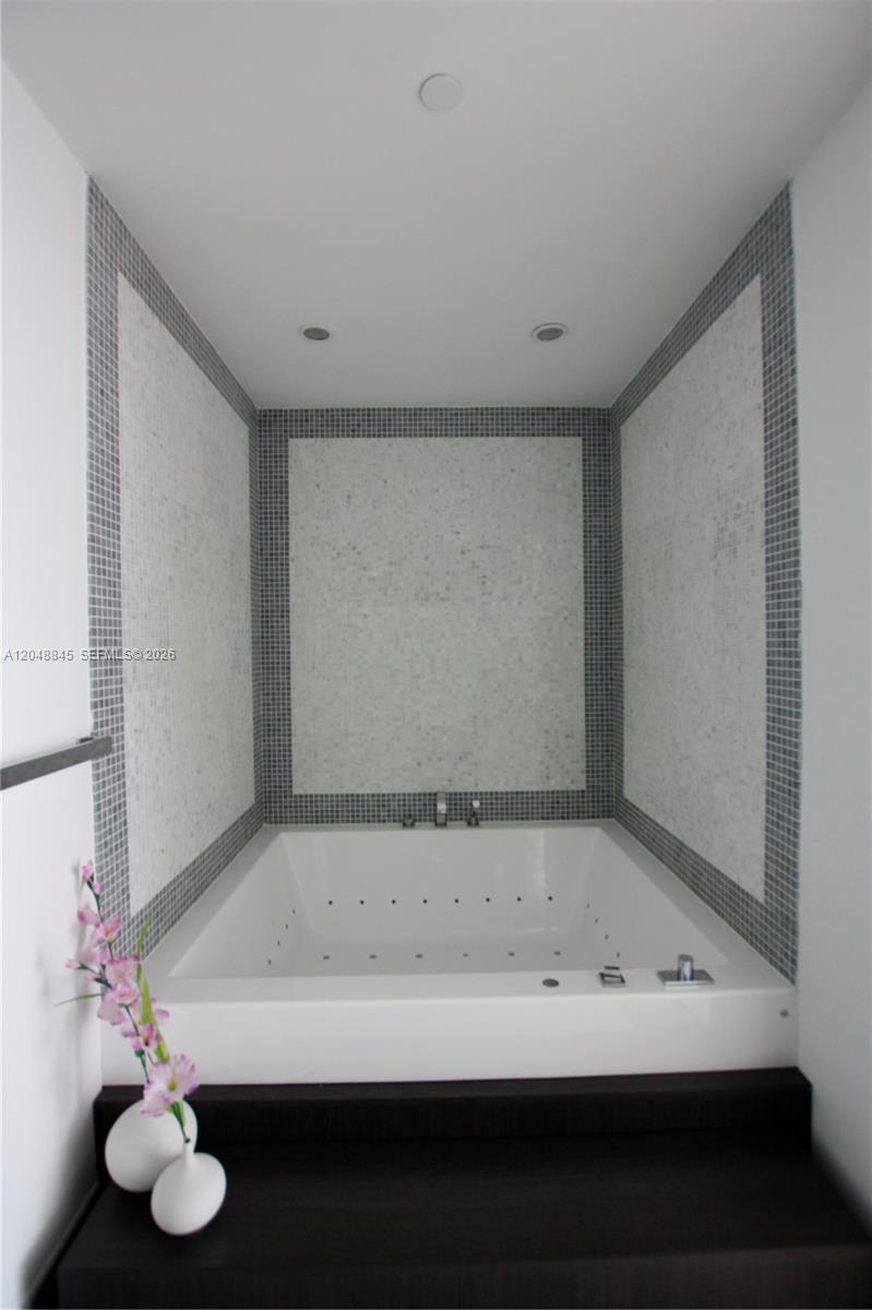 A white jetted bathtub is set in a tiled alcove with gray mosaic accents — 200 Biscayne Boulevard Way # 3209, Miami FL 33131, MIAMI, FL