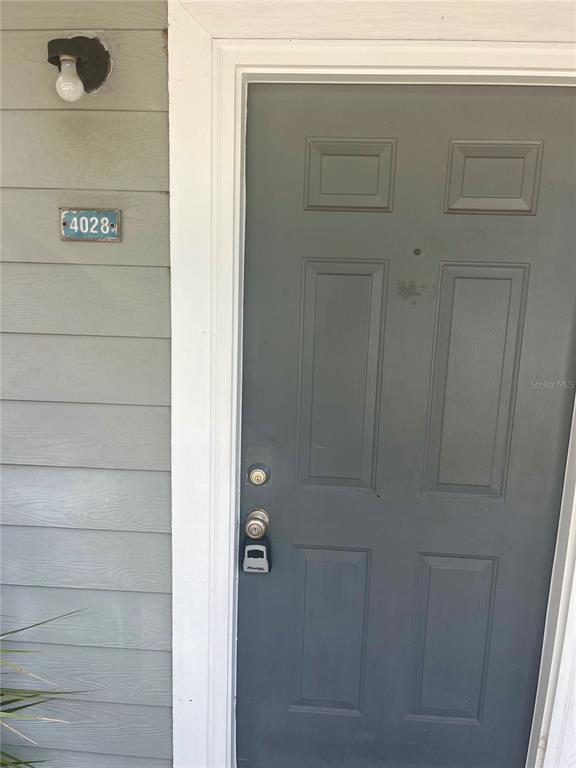 A gray front door with a lockbox is situated next to a light fixture and address plaque — 2905 SW ARCHER ROAD UNIT T4028, GAINESVILLE, FL