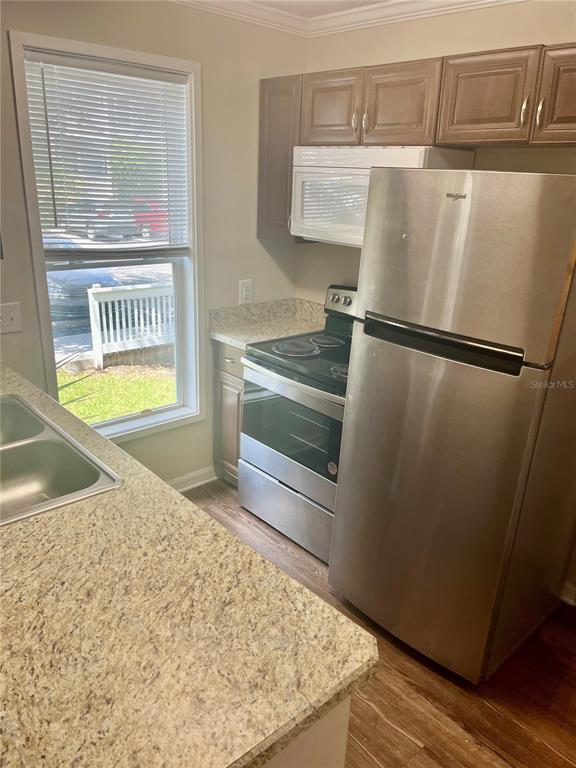 A kitchen features stainless steel appliances, wood-toned cabinets, and granite countertops next to a window — 2905 SW ARCHER ROAD UNIT T4028, GAINESVILLE, FL