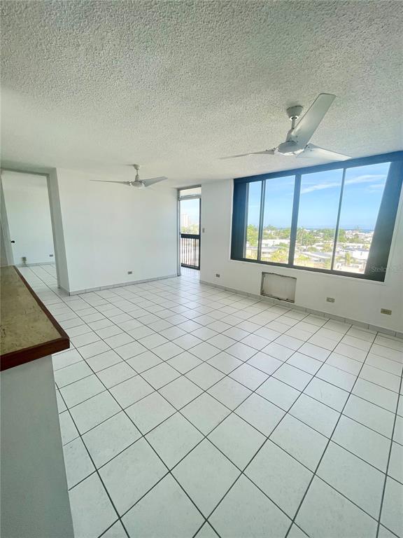 An open living area features white tile flooring, two ceiling fans, and large windows — 1 INGA STREET UNIT 6F, SAN JUAN, PR