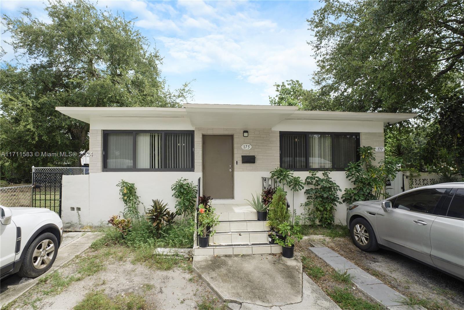 The exterior of a single-story house features a light-colored facade, a central entrance, and two cars — 175 NW 68th St, Miami FL 33150, MIAMI, FL