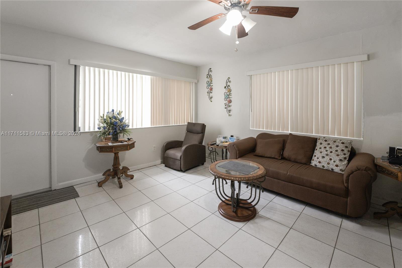 A living room features white tile flooring, a brown sofa, a recliner, and vertical blinds — 175 NW 68th St, Miami FL 33150, MIAMI, FL