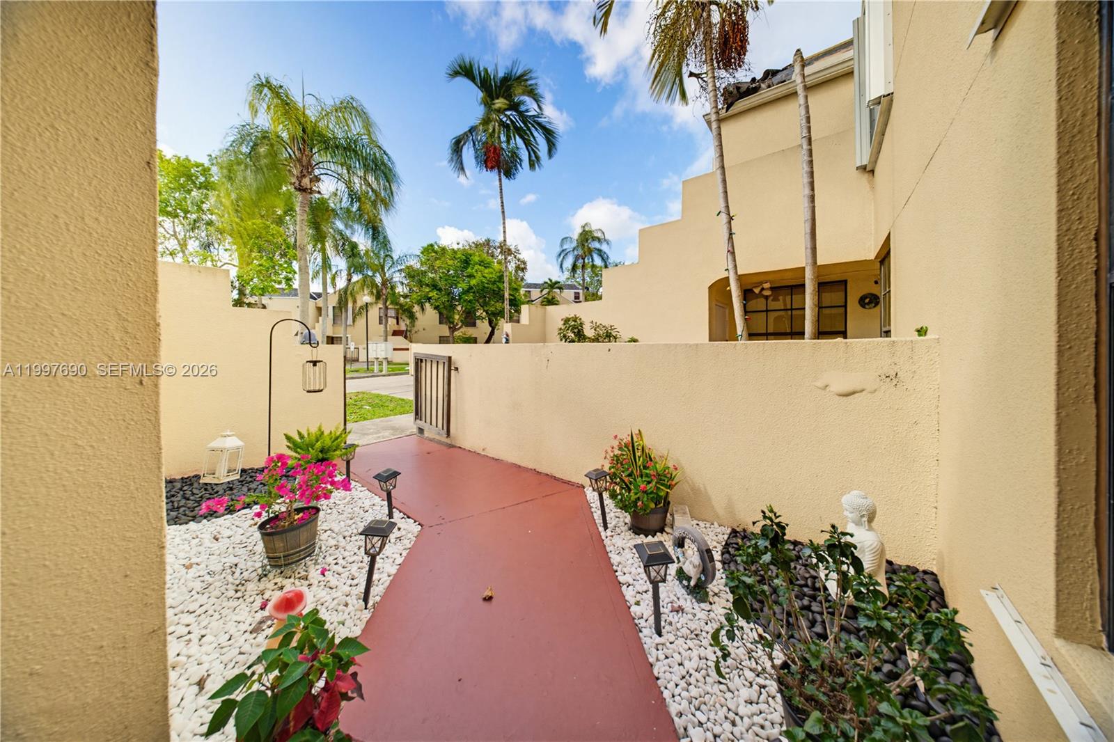 A paved walkway leads through a courtyard with white gravel, potted plants, and a gate — 12984 SW 88th Ln # B104, Miami FL 33186, MIAMI, FL