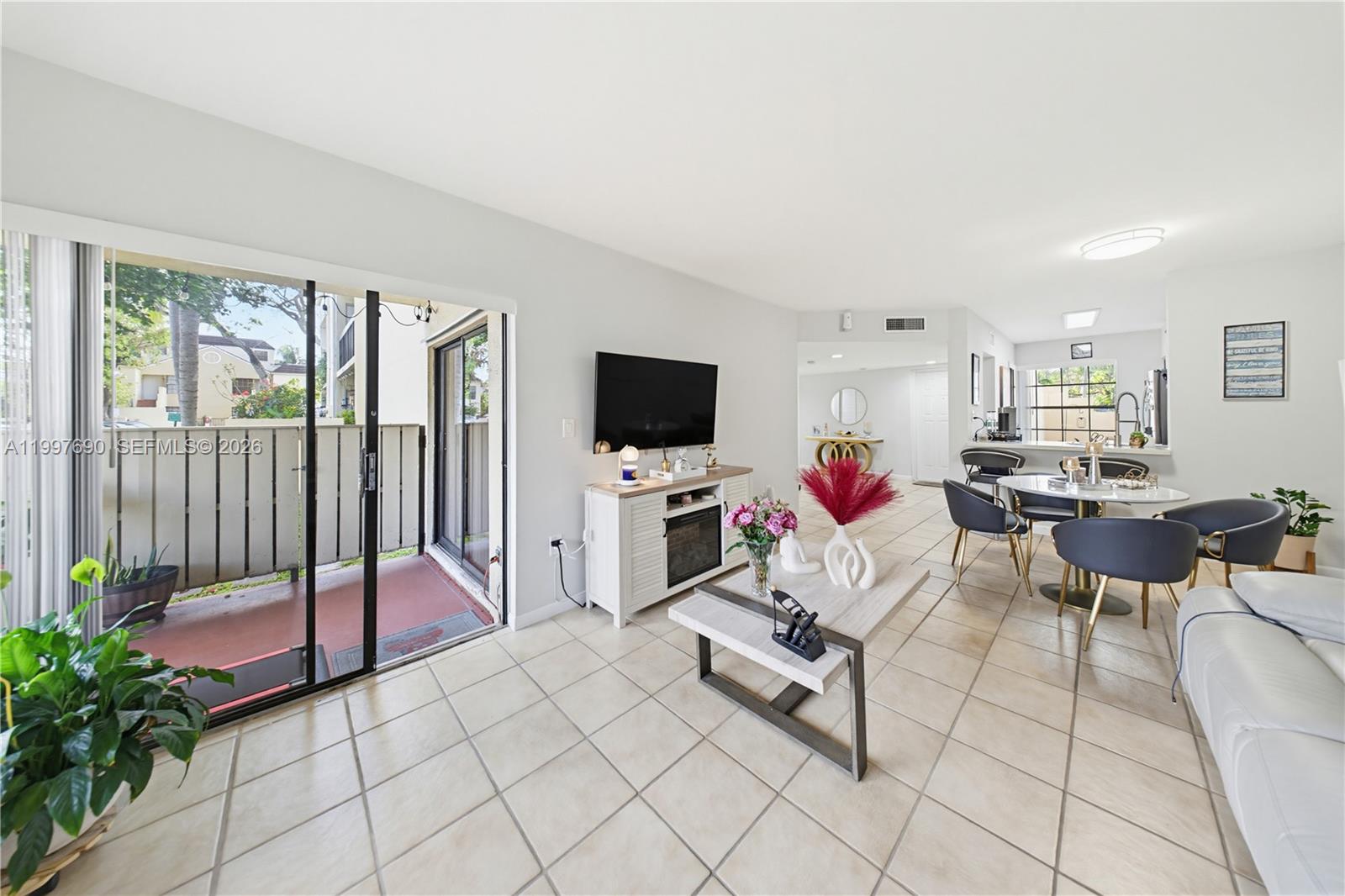 A living and dining area features tile flooring, a television console, and a sliding glass door — 12984 SW 88th Ln # B104, Miami FL 33186, MIAMI, FL