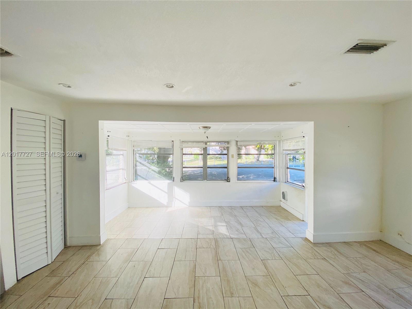 A bright, empty room features light-colored wood-look tile flooring and large windows overlooking a street — 2230 NW 51st Terrace # 1, Miami FL 33142, MIAMI, FL