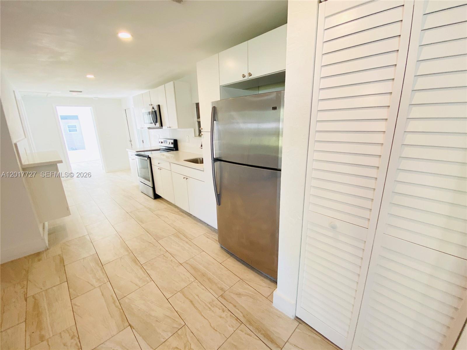 A kitchen features white cabinetry, stainless steel appliances, and light-colored tile flooring — 2230 NW 51st Terrace # 1, Miami FL 33142, MIAMI, FL