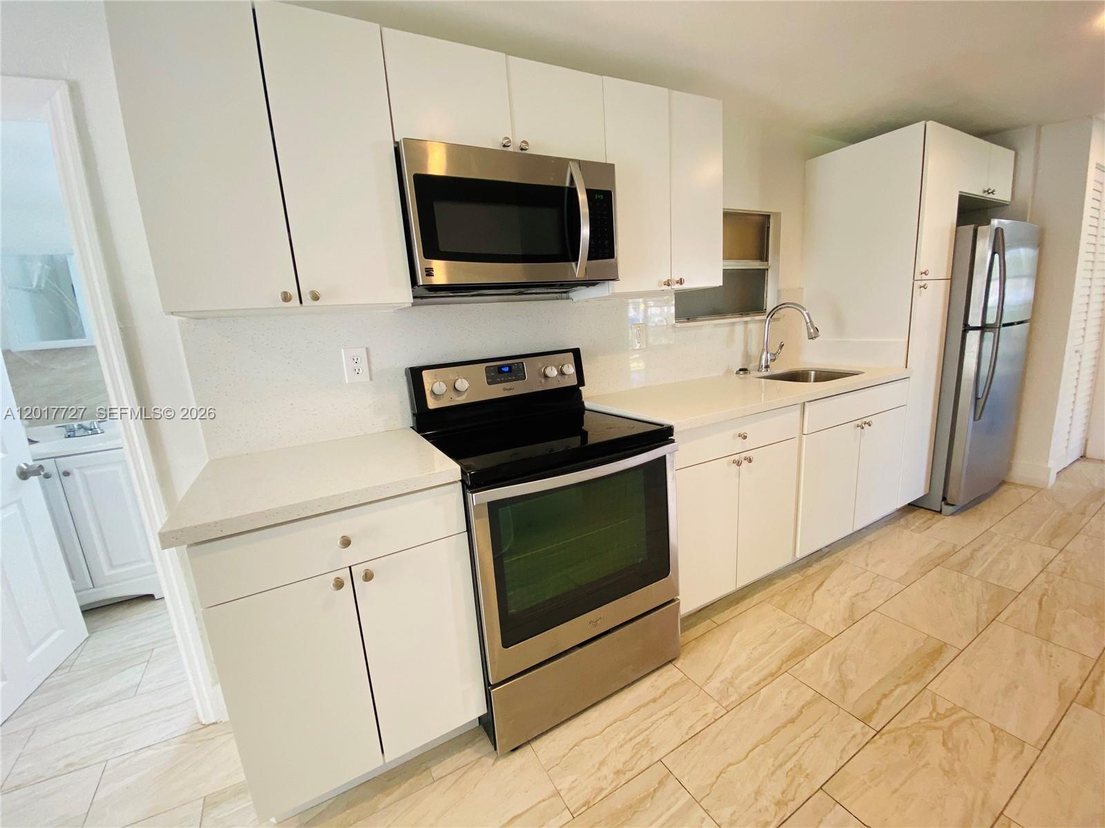 A kitchen features white cabinets, stainless steel appliances, and light-colored countertops and flooring — 2230 NW 51st Terrace # 1, Miami FL 33142, MIAMI, FL