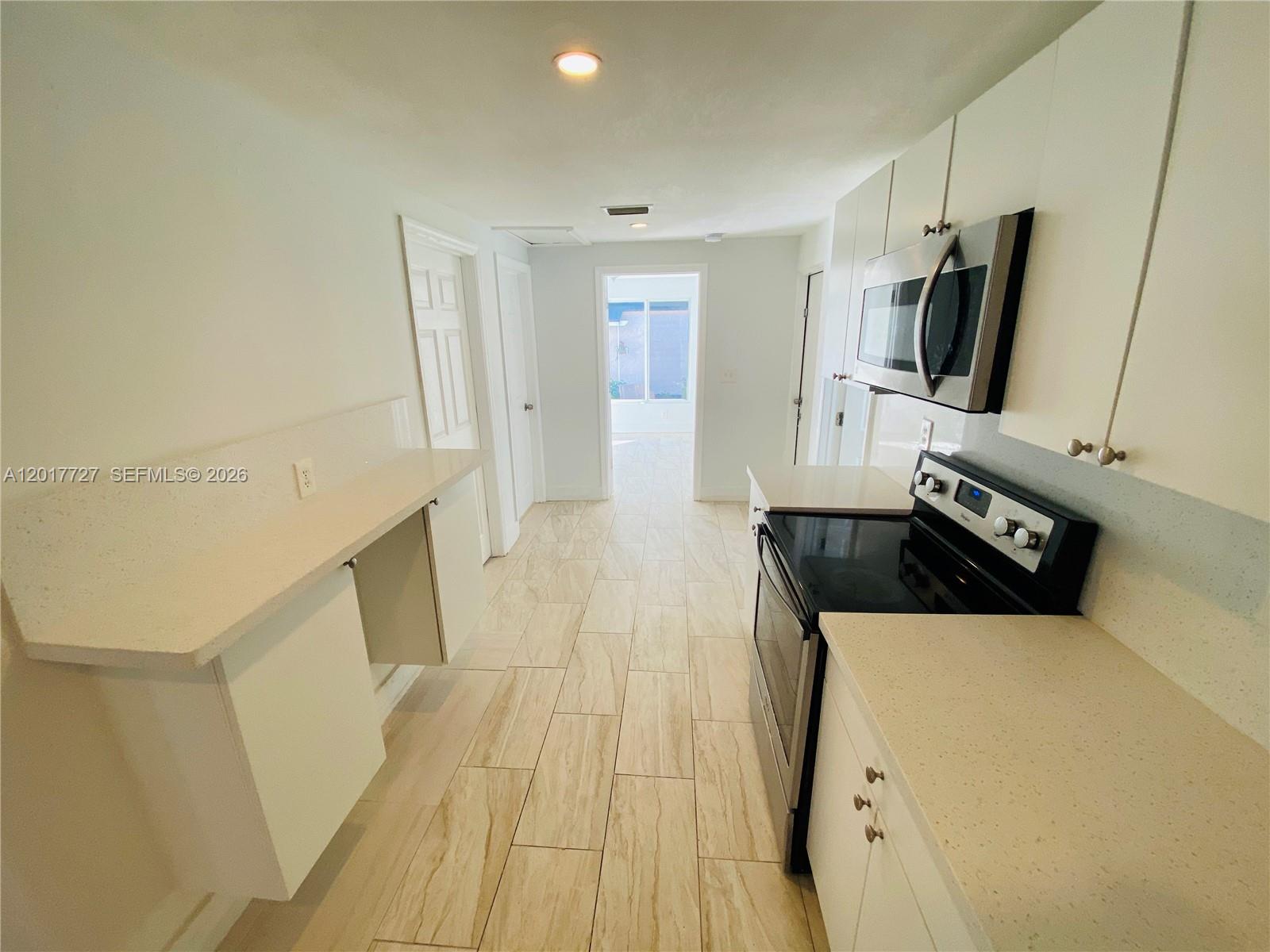 A galley-style kitchen features white cabinets, light countertops, and wood-look tile flooring — 2230 NW 51st Terrace # 1, Miami FL 33142, MIAMI, FL