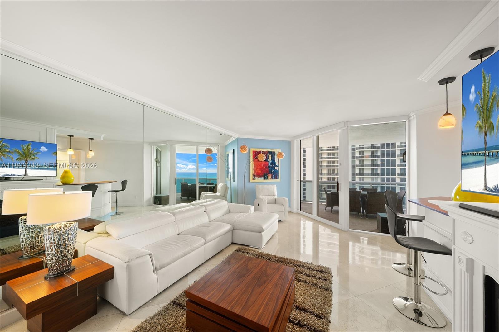 A living room features a white sectional sofa, a mirrored wall, and a balcony view — 4775 Collins Ave # 1708, Miami Beach FL 33140, MIAMI BEACH, FL