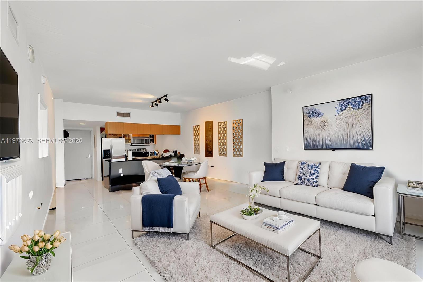 A bright living room features white tile floors, a white sofa, and an open kitchen — 1750 N Bayshore Dr # 2510, Miami FL 33132, MIAMI, FL