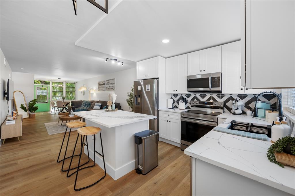 A modern kitchen with white cabinets and marble countertops opens into a living area — 1433 S BELCHER ROAD UNIT F9, CLEARWATER, FL