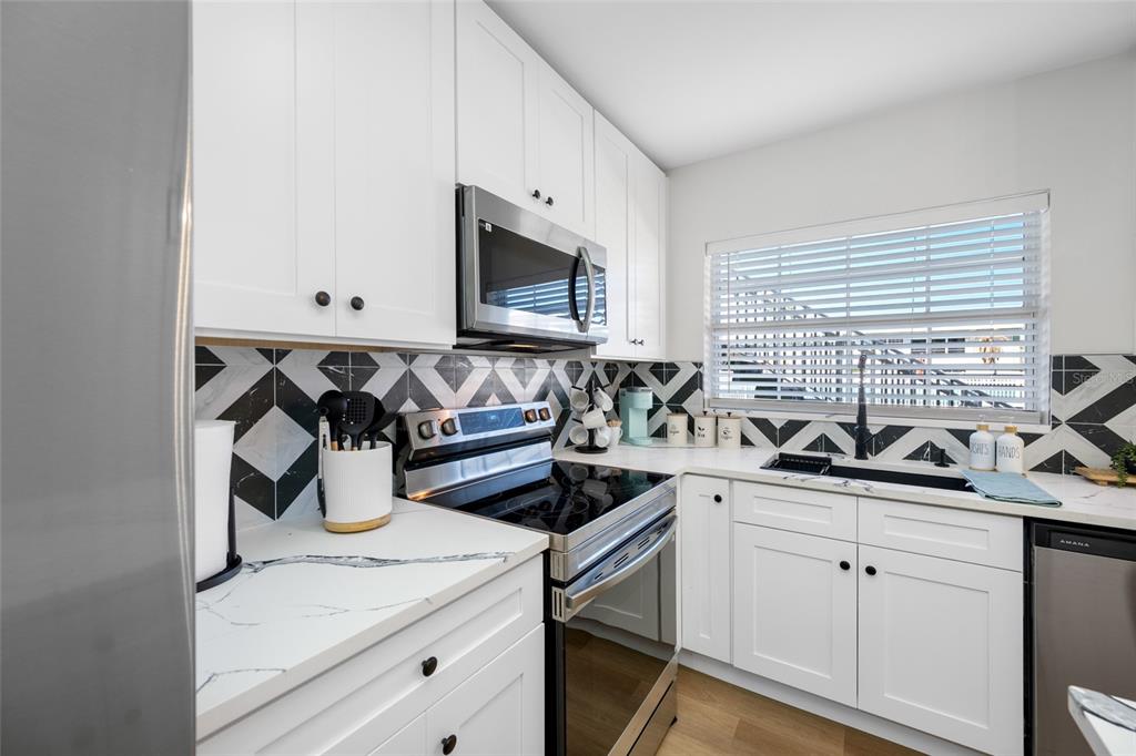 A kitchen features white cabinets, a geometric tile backsplash, stainless steel appliances, and quartz countertops — 1433 S BELCHER ROAD UNIT F9, CLEARWATER, FL