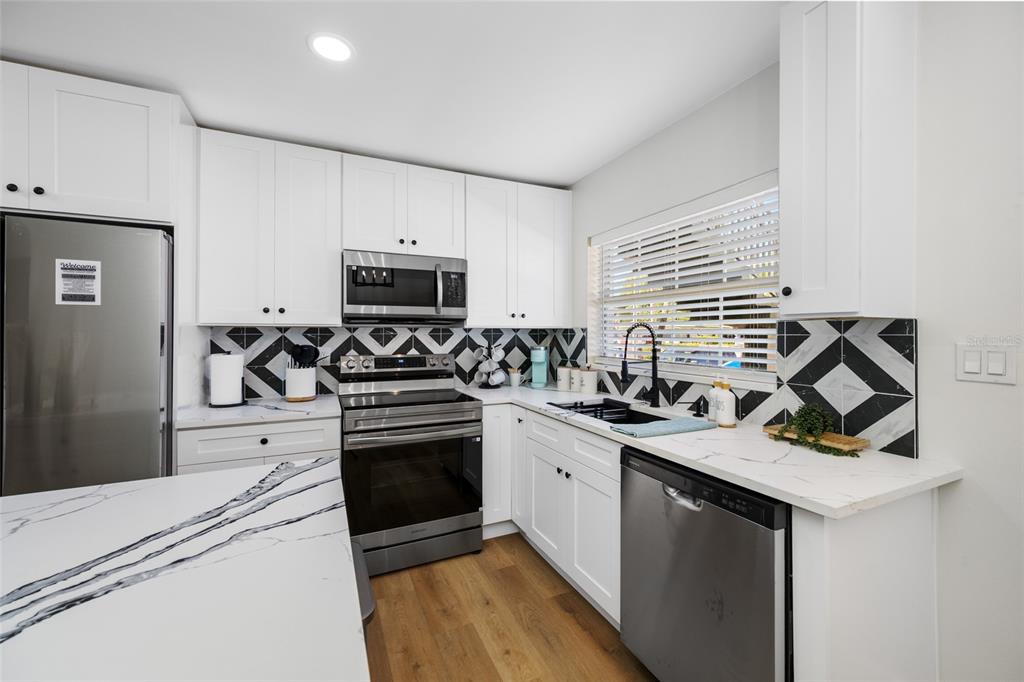 A modern kitchen features white cabinets, stainless steel appliances, and a bold geometric tile backsplash — 1433 S BELCHER ROAD UNIT F9, CLEARWATER, FL