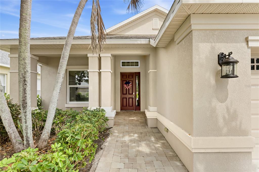 A paved walkway leads to the front entrance of a beige house with a brown door — 3631 SUMMERWIND CIRCLE, BRADENTON, FL