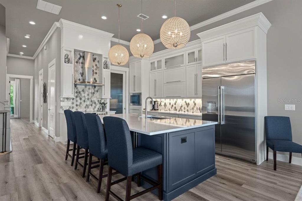 A modern kitchen features a dark blue island, white cabinetry, stainless steel appliances, and pendant lighting — 18 SPINAKER CIRCLE, PALM COAST, FL