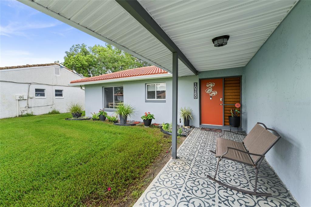 A covered porch with patterned tile flooring leads to an orange front door — 10760 WILDERNESS COURT, ORLANDO, FL