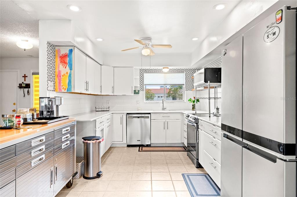 A kitchen features white cabinets, stainless steel appliances, a rolling metal island, and tile flooring — 10760 WILDERNESS COURT, ORLANDO, FL