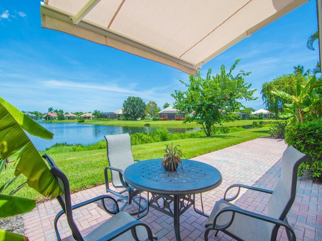 A patio with a table and chairs overlooks a lake and green lawn under an awning — 1208 Riverwind Circle, Vero Beach FL 32967, VERO BEACH, FL