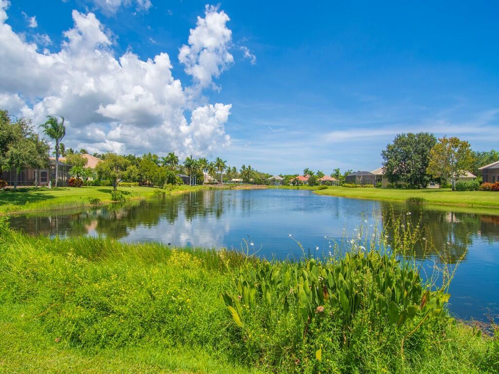 A pond sits in the center of a residential neighborhood with green lawns and palm trees — 1208 Riverwind Circle, Vero Beach FL 32967, VERO BEACH, FL