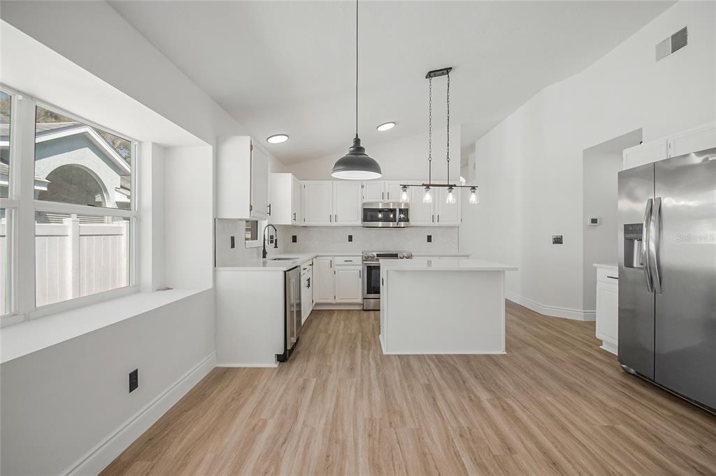 A modern kitchen features white cabinets, stainless steel appliances, a center island, and wood flooring — 808 WHITE IVEY COURT, APOPKA, FL