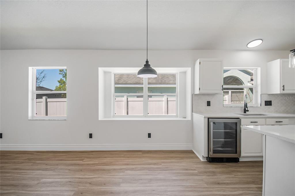 A bright kitchen and dining area with white cabinets, wood-look flooring, and a pendant light — 808 WHITE IVEY COURT, APOPKA, FL