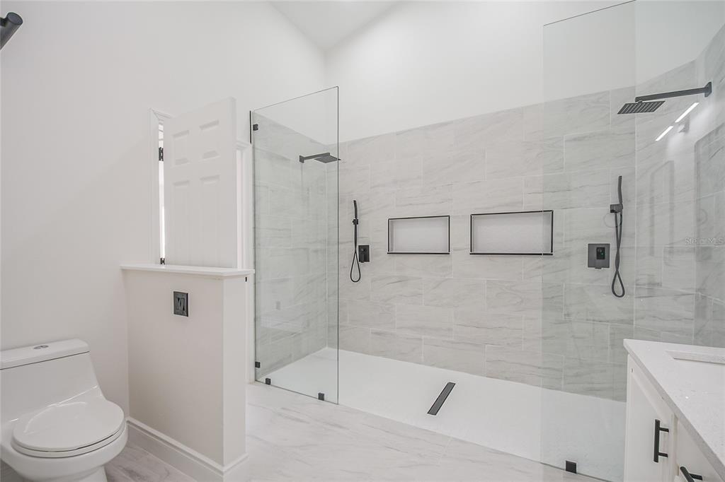 A modern bathroom features a walk-in shower with glass walls, dual showerheads, and marble-look tile — 808 WHITE IVEY COURT, APOPKA, FL