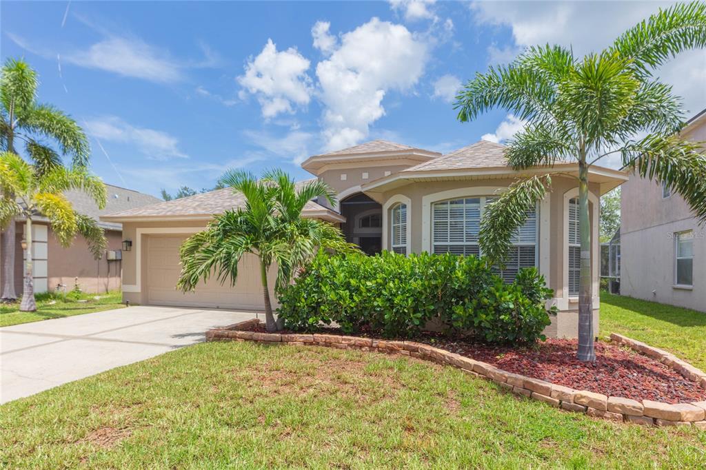 A single-story tan house with a two-car garage, palm trees, and a stone-bordered garden bed — 1615 BONITA BLUFF COURT, RUSKIN, FL