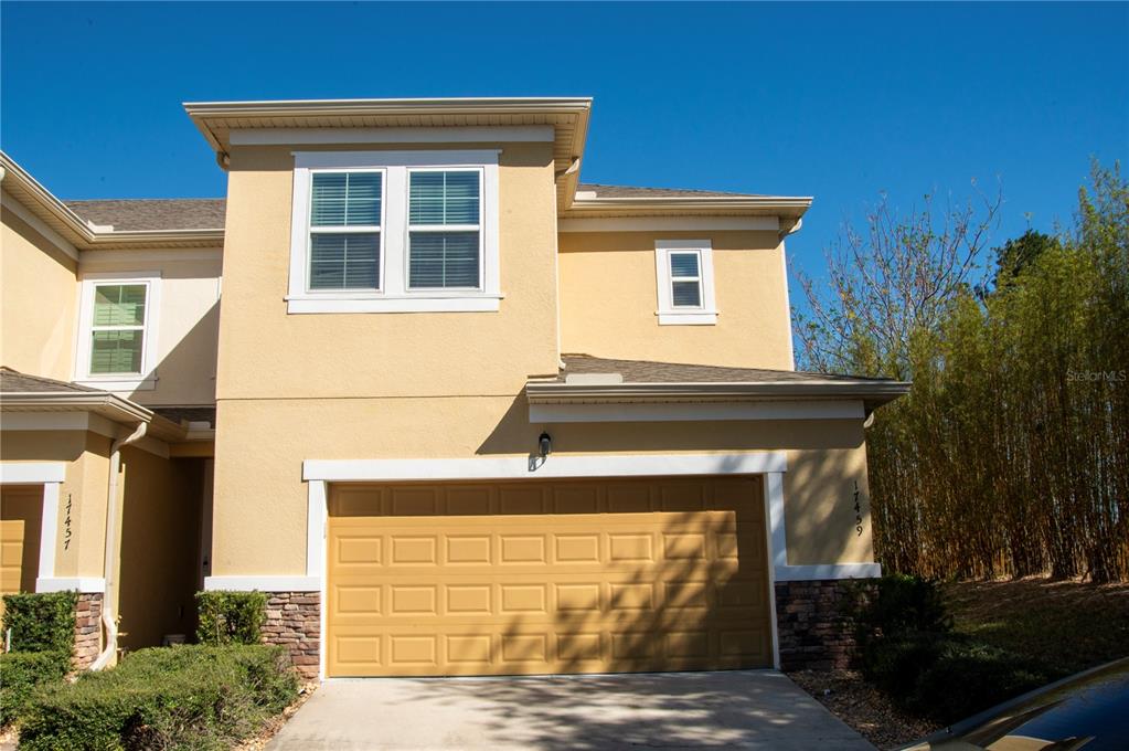 A two-story tan stucco townhouse features a two-car garage and a stone veneer base — 17459 CHATEAU PINE WAY, CLERMONT, FL