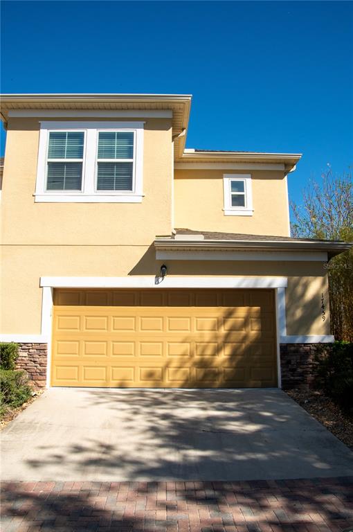 A two-story house exterior features a tan stucco facade, a double garage, and stone accents — 17459 CHATEAU PINE WAY, CLERMONT, FL