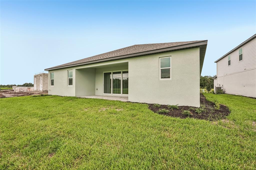 The rear exterior of a single-story house features a covered patio and a grassy yard — 3664 142ND TERRACE E, BRADENTON, FL
