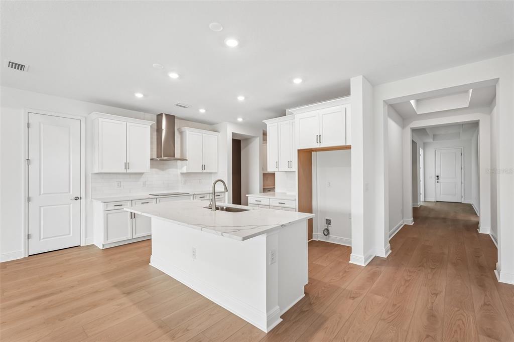 A modern kitchen features white cabinets, a marble-topped island, and light wood flooring — 3664 142ND TERRACE E, BRADENTON, FL