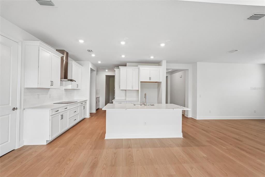 A modern kitchen features white cabinets, a central island, and light wood flooring — 3664 142ND TERRACE E, BRADENTON, FL