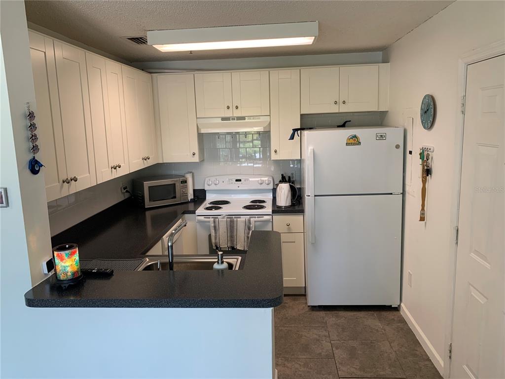 A kitchen features white cabinets, black countertops, a white stove, and a white refrigerator — 4049 CROCKERS LAKE BOULEVARD UNIT 25, SARASOTA, FL