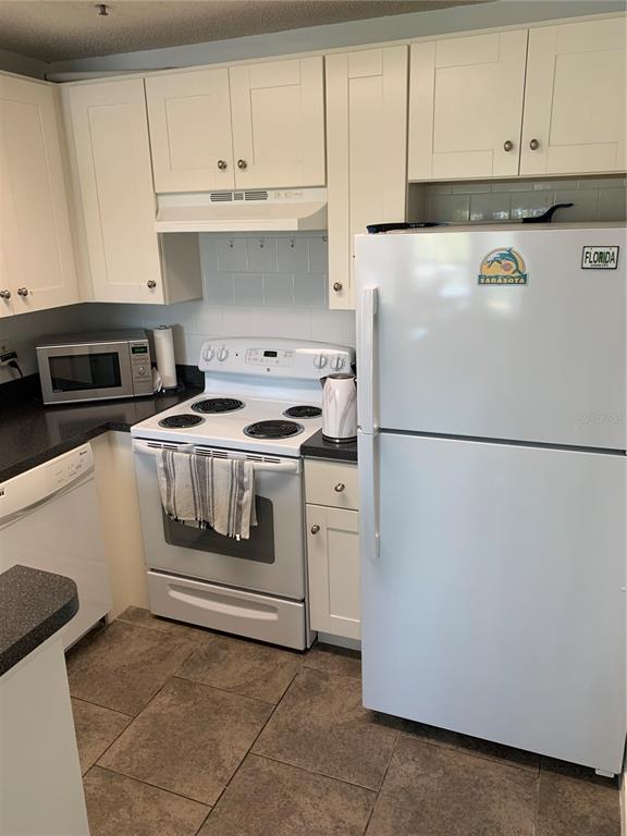 A kitchen features white cabinets, a white stove, a white refrigerator, and dark countertops — 4049 CROCKERS LAKE BOULEVARD UNIT 25, SARASOTA, FL