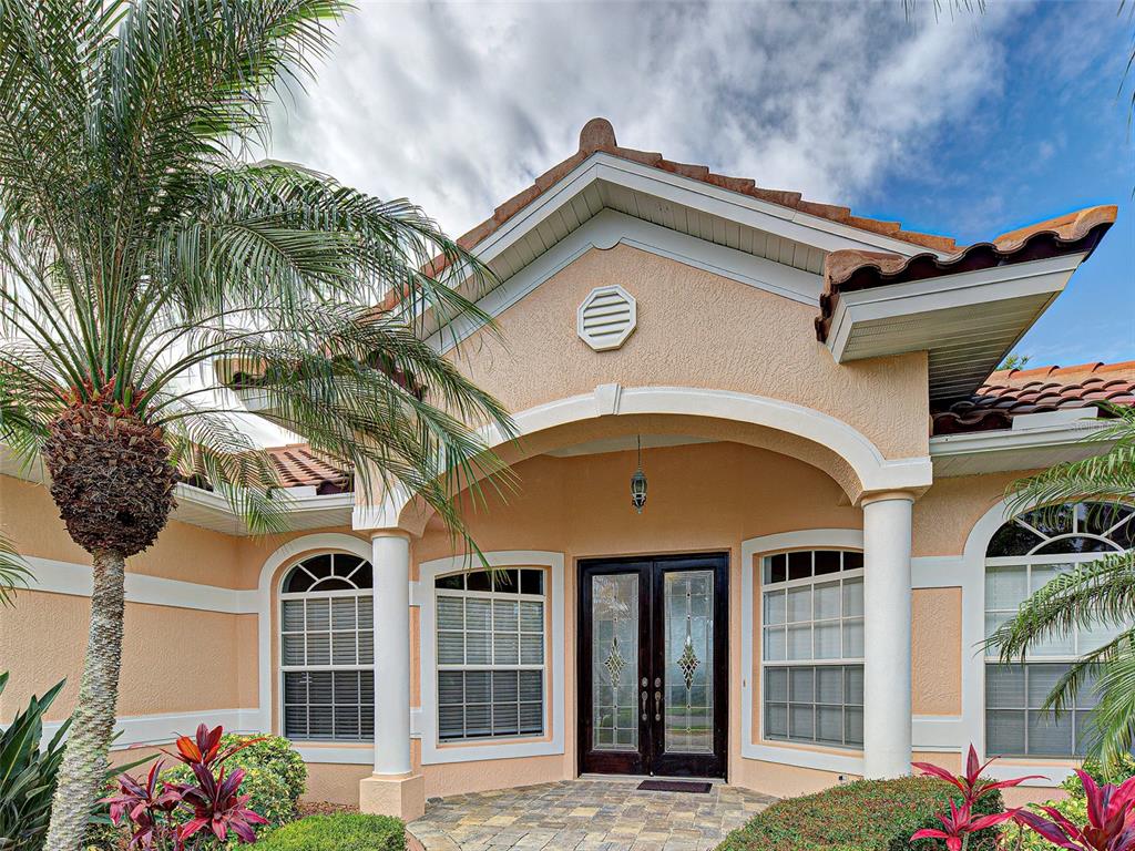The exterior of a peach-colored house features a covered entryway with white columns and double doors — 5017 BELLA TERRA DRIVE, VENICE, FL