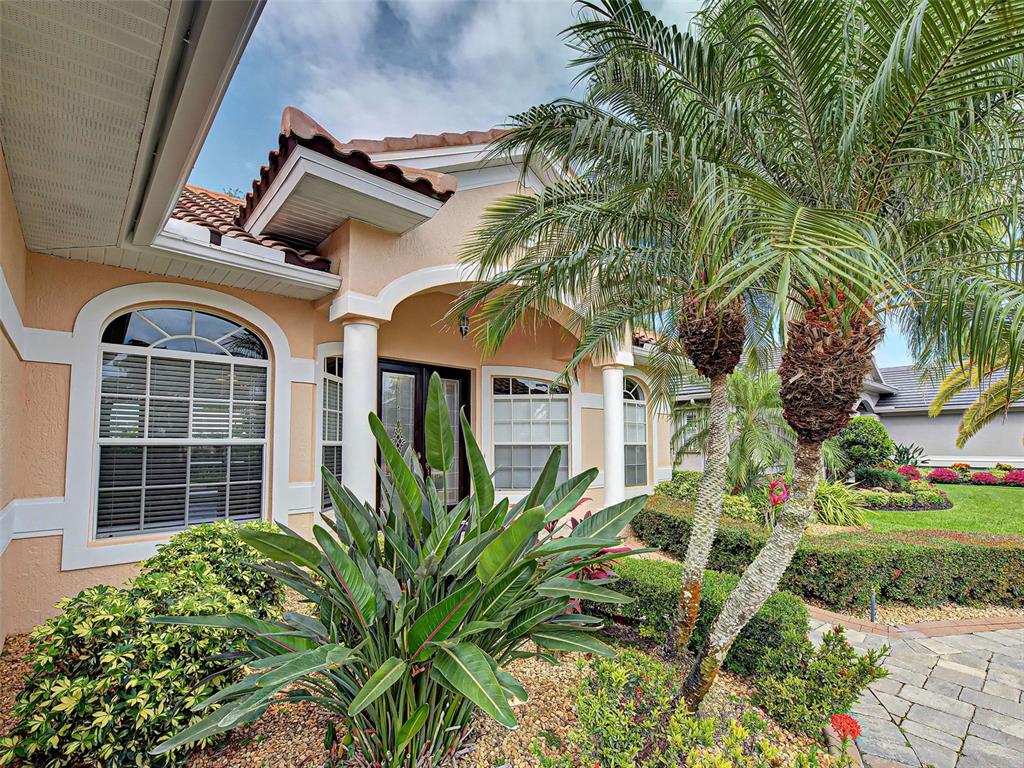 A peach-colored house exterior features a covered entryway with white columns and palm trees — 5017 BELLA TERRA DRIVE, VENICE, FL