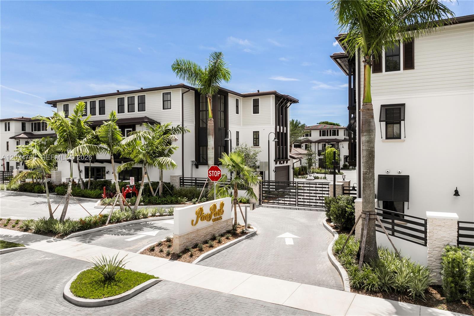 The exterior view shows the gated entrance to a residential complex with modern white buildings — 7504 SW 100th St, Pinecrest FL 33156, PINECREST, FL