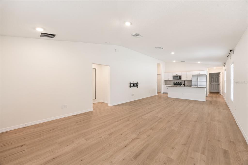 An open-concept living area with light wood-look flooring leads to a kitchen with white cabinets — 12401 STREAMBED DRIVE, RIVERVIEW, FL