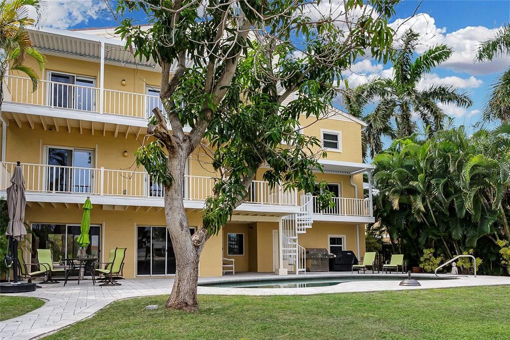 A three-story yellow house features stacked balconies, a spiral staircase, and a backyard swimming pool — 614 NORTON STREET, LONGBOAT KEY, FL