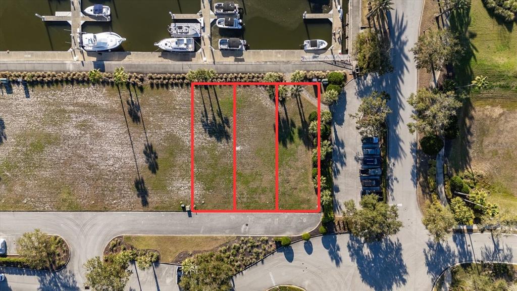 This aerial view shows three adjacent vacant lots situated next to a marina and road — 100 HARBOR VILLAGE POINT S, PALM COAST, FL