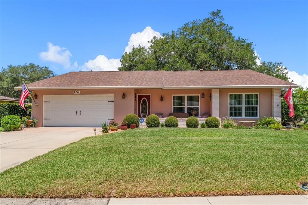 A single-story house with a pink exterior, a two-car garage, and a manicured front lawn — 2211 PORTSIDE PASSAGE, PALM HARBOR, FL