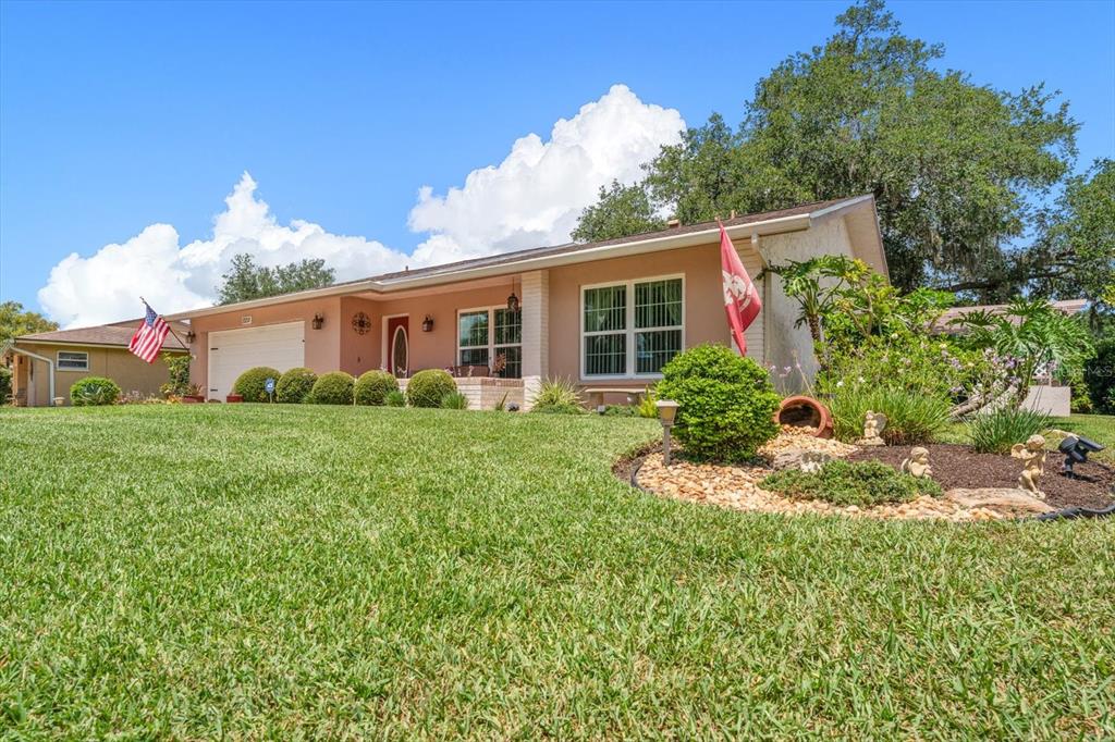 A single-story house with a tan exterior, a two-car garage, and a landscaped front yard — 2211 PORTSIDE PASSAGE, PALM HARBOR, FL