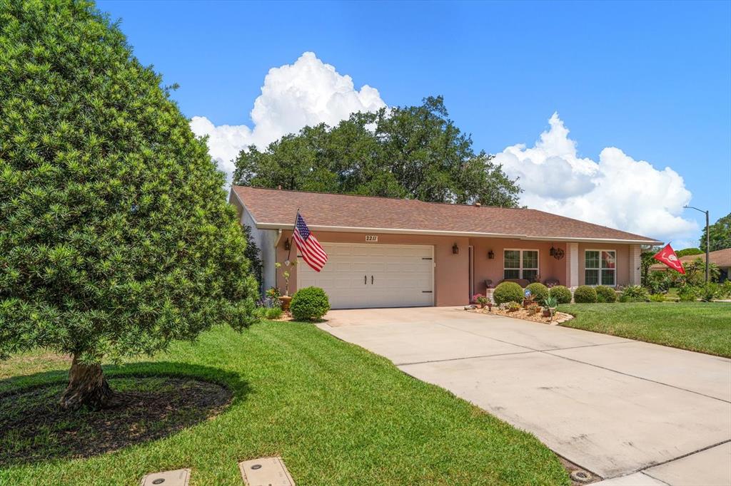 A single-story house with a tan exterior, a two-car garage, and a manicured front lawn — 2211 PORTSIDE PASSAGE, PALM HARBOR, FL