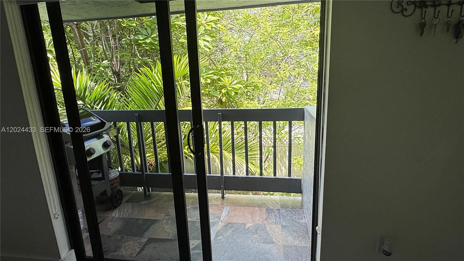 A sliding glass door opens onto a tiled balcony with a grill and lush greenery — 13675 SW 62nd St # 3, Miami FL 33183, MIAMI, FL