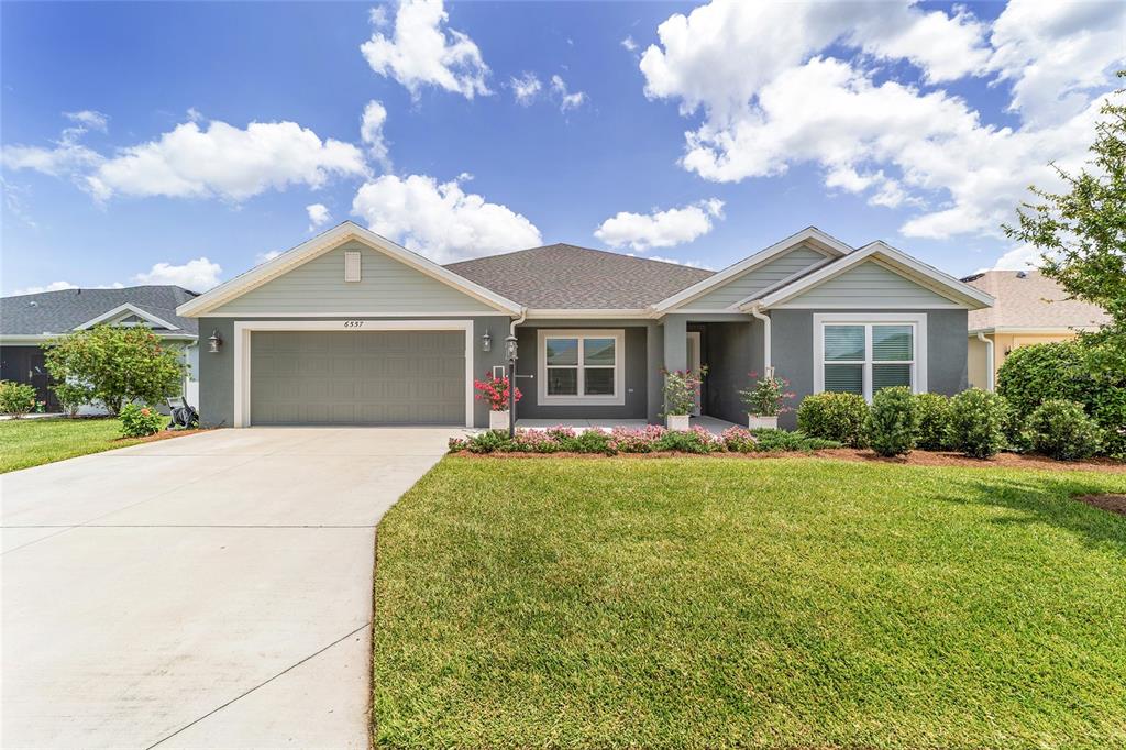 A single-story suburban house with a two-car garage, gray siding, and a manicured lawn — 6557 MCKNIGHT LOOP, THE VILLAGES, FL