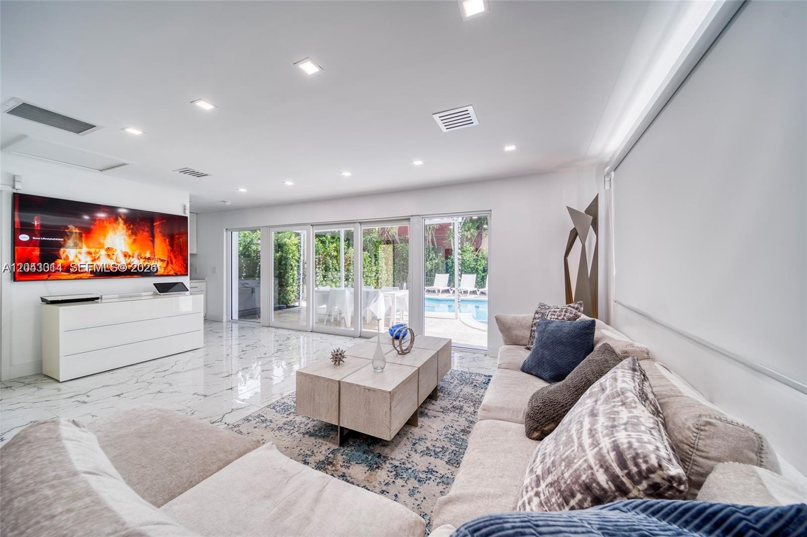 A modern living room features marble floors, a large television, and sliding glass doors to a pool — 2298 SW 16th Ave, Miami FL 33145, MIAMI, FL
