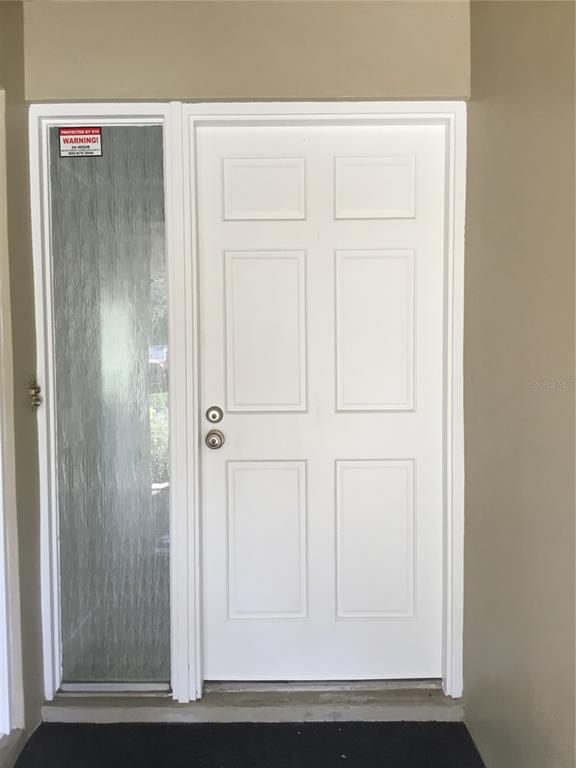A white six-panel front door with a vertical glass sidelight sits in a tan entryway — 44 COUNTRY CLUB DRIVE UNIT 44, LARGO, FL